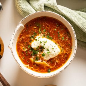 Lasagna soup in a bowl with a dollop of ricotta garnished with parsley and parmesan.