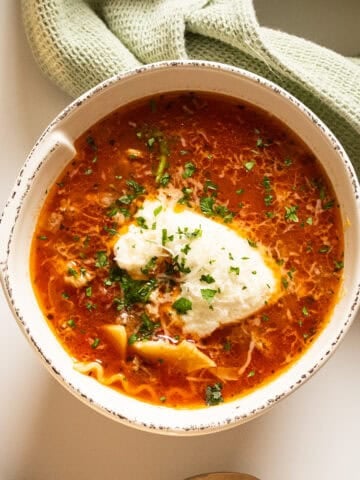 Lasagna soup in a bowl with a dollop of ricotta garnished with parsley and parmesan.