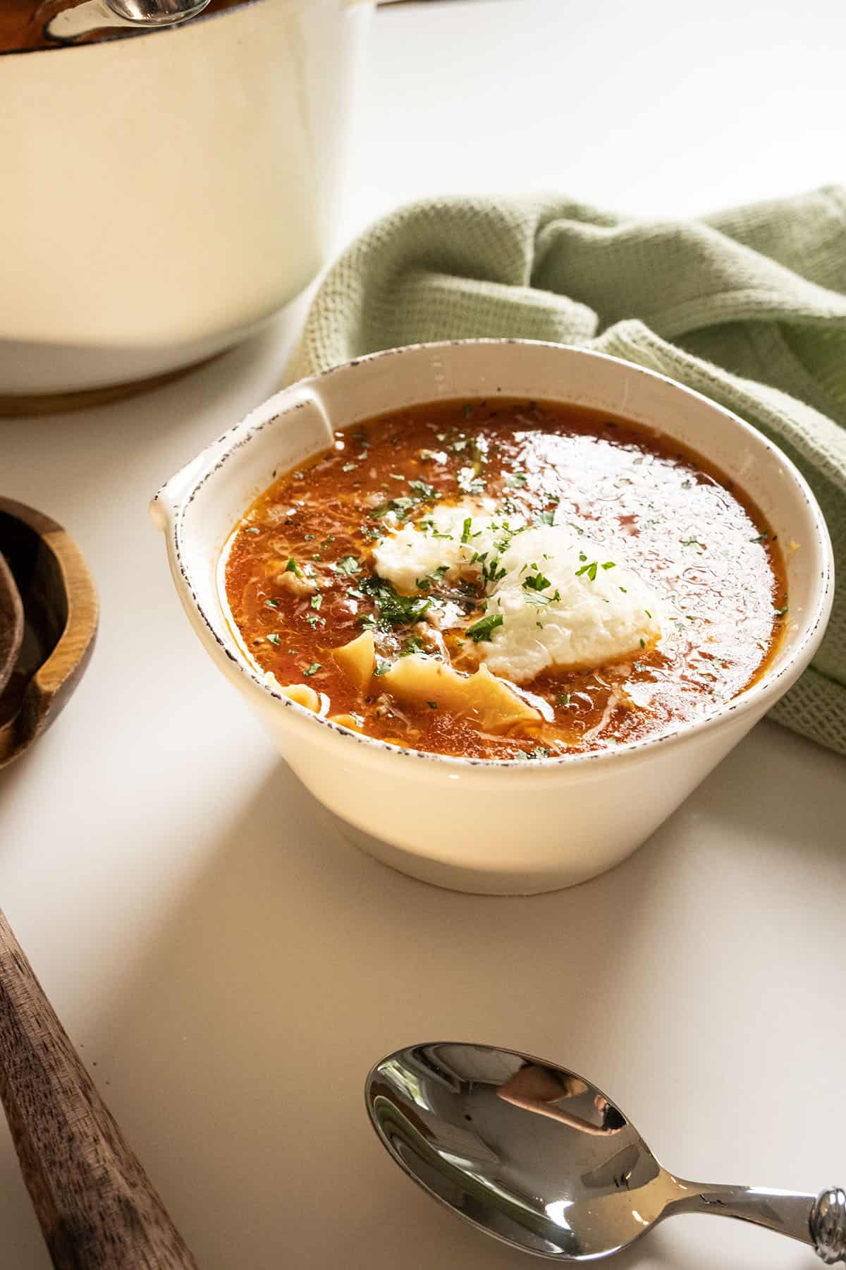 Lasagna soup in a bowl with a dollop of ricotta topped with parsley and parmesan.