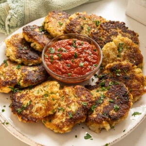 Fried cauliflower cakes on a plate with marinara sauce.