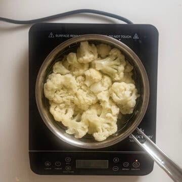 Cauliflower in steamer basket in a pot.