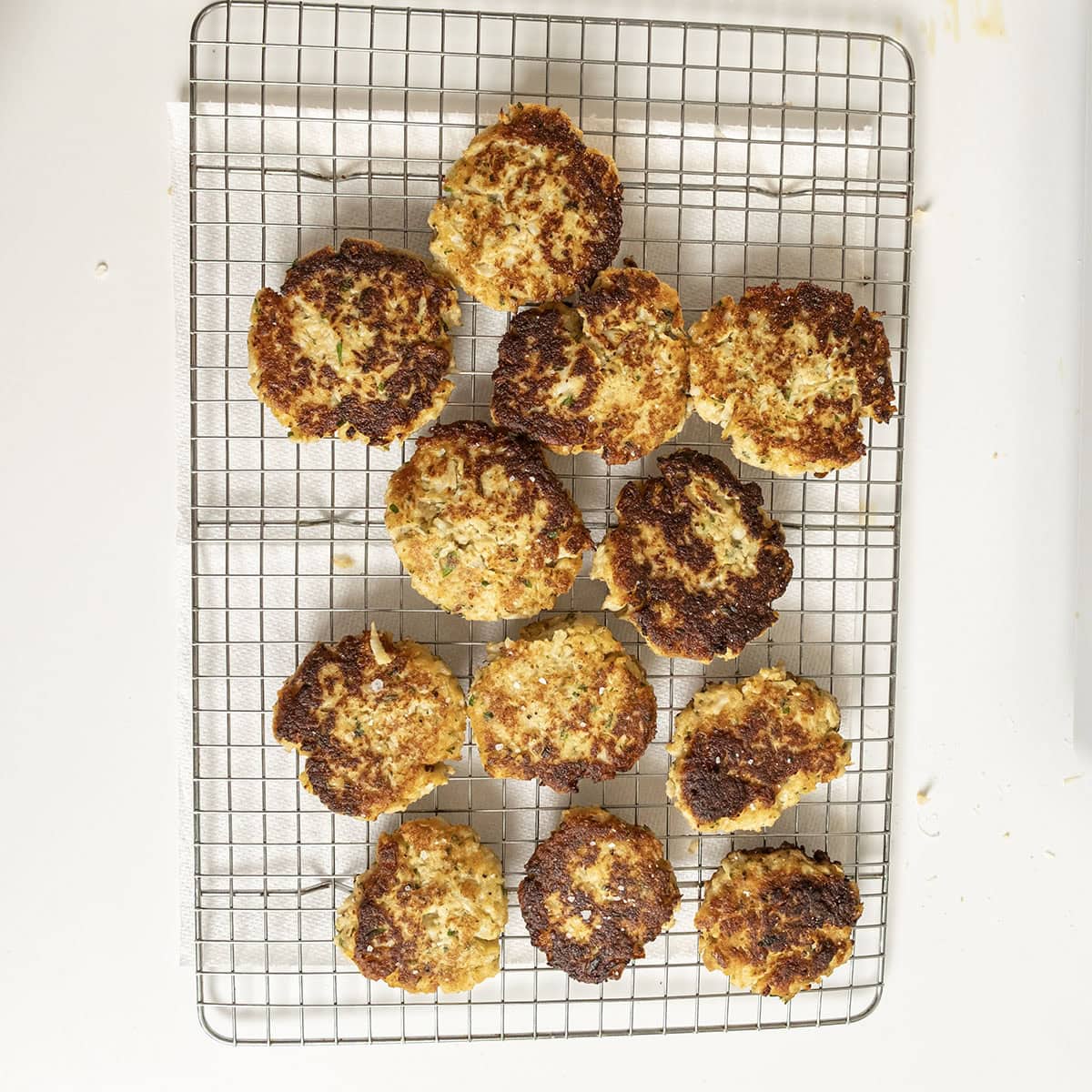 Fried cauliflower cakes on a cooling rack, sprinkled with salt.