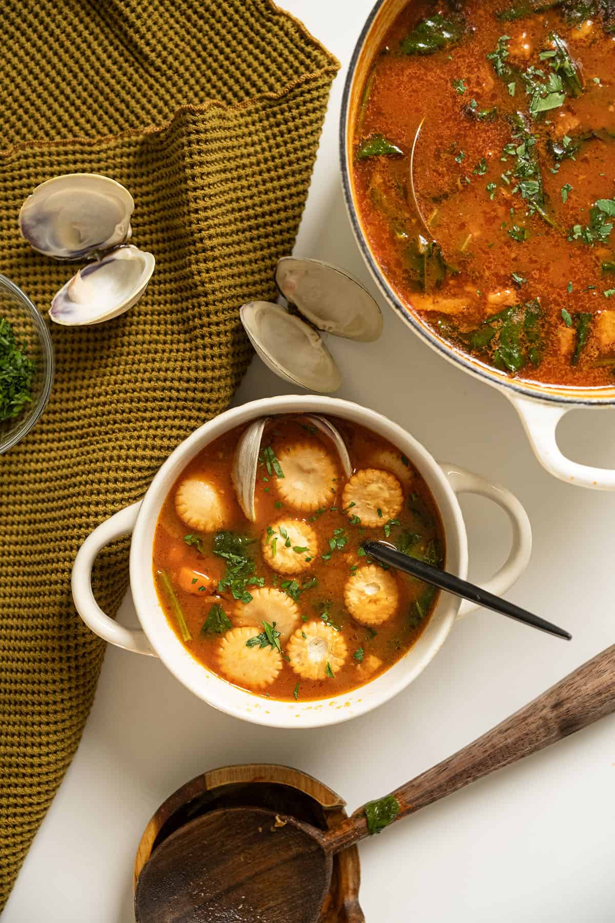Manhattan clam chowder topped with oyster crackers, next to the pot of soup.