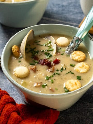 New england clam chowder in a bowl garnished with chives and oyster crackers.