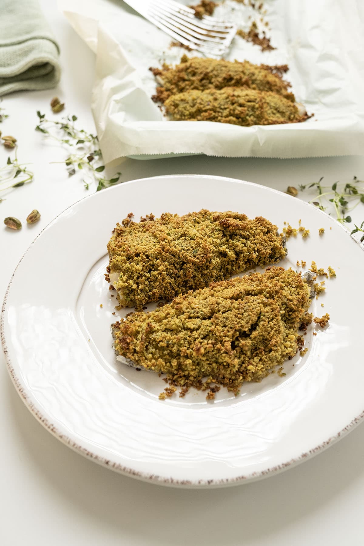 Pistachio crusted sea bass on a plate and baking tray.