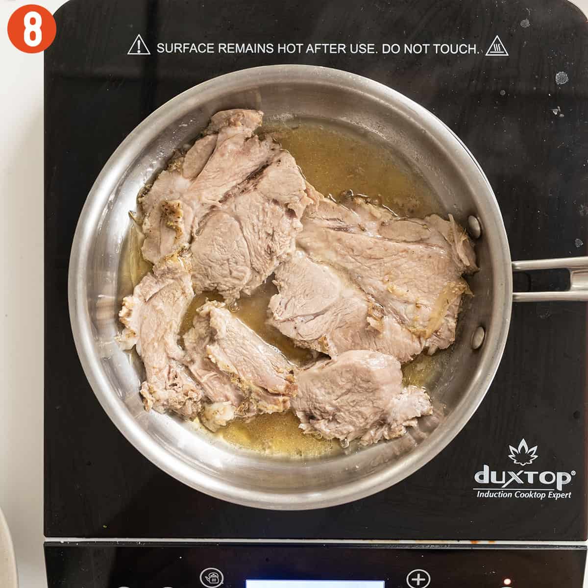 Heating sliced pork shoulder in a pan with pork au jus.