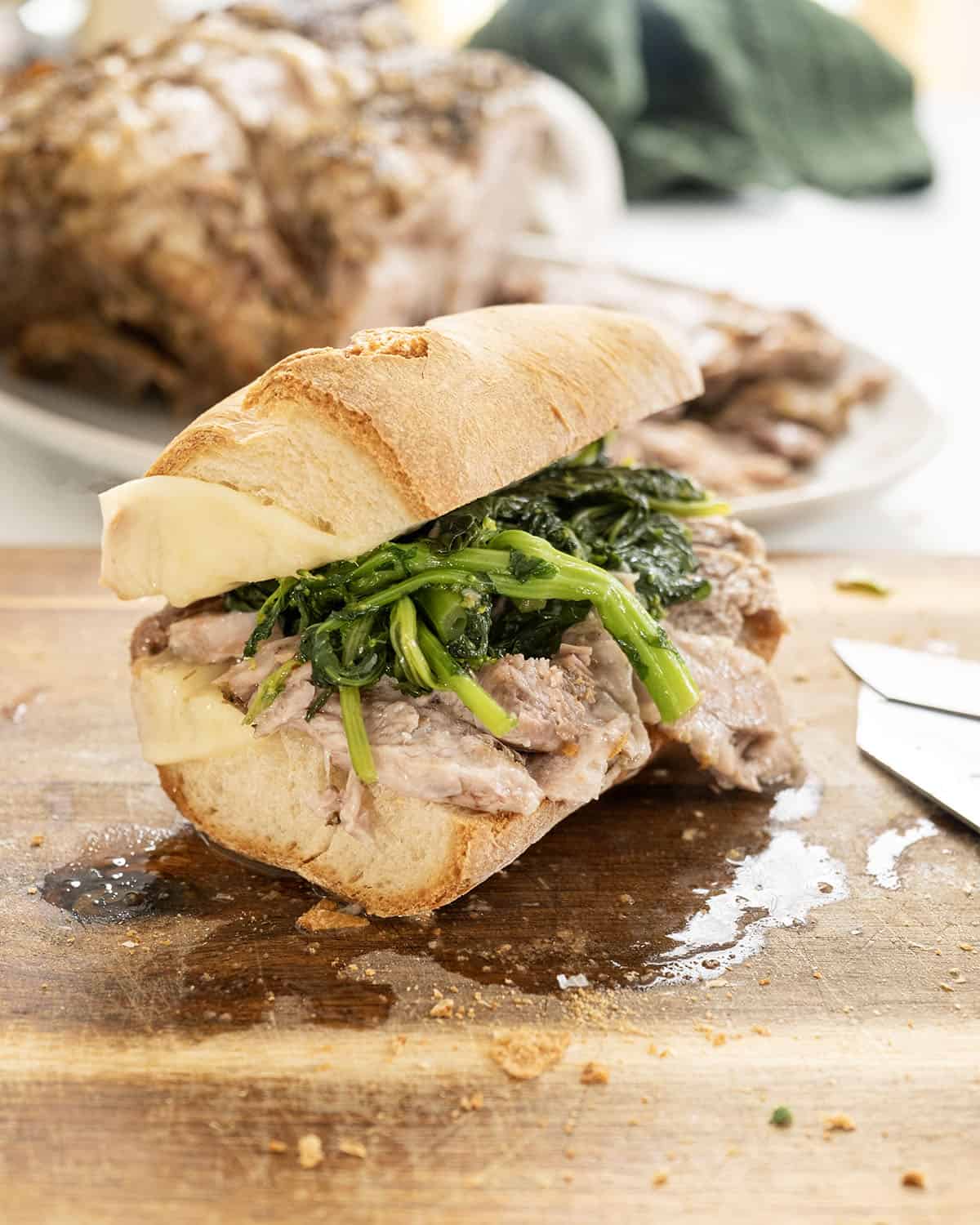 Sliced pork shoulder on a sandwich with broccoli rabe and provolone.