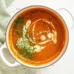 Roasted red pepper soup drizzled with cream and garnished with parsley.