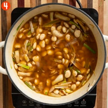 Simmering broad beans and spring onions in a pot.