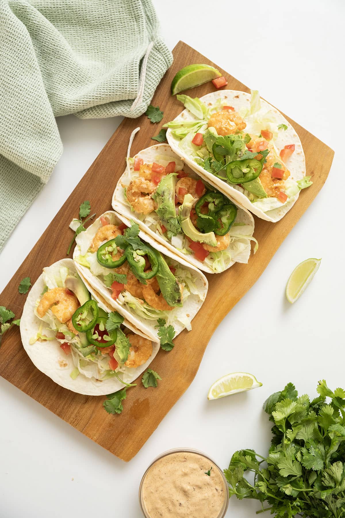 Volcano shrimp tacos on a cutting board topped with cilantro, tomatoes, jalapeno, and avocado.