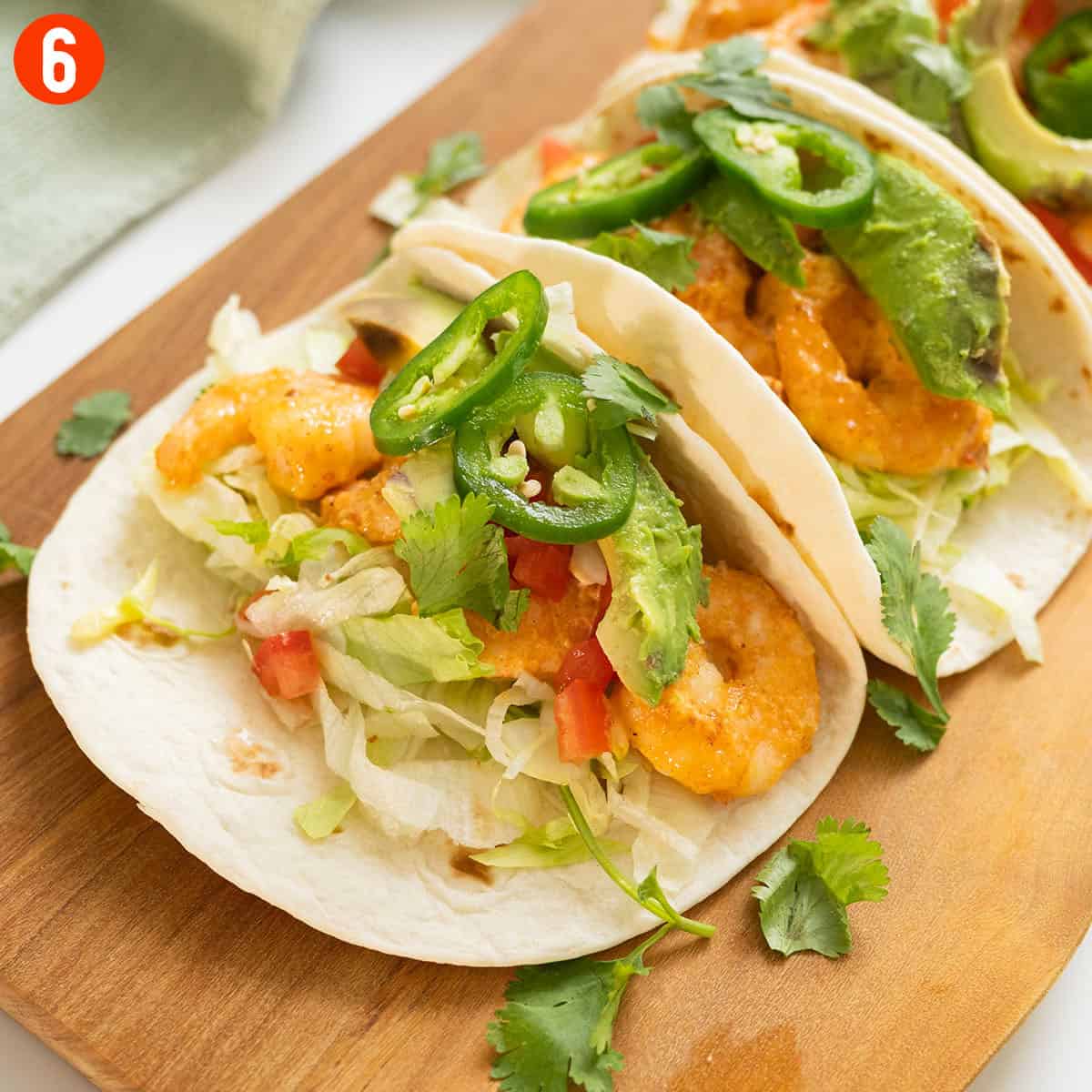 Volcano shrimp tacos on a cutting board topped with cilantro, tomatoes, jalapeno, and avocado.