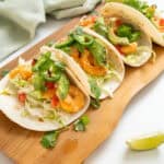Volcano shrimp tacos on a cutting board topped with cilantro, tomatoes, jalapeno, and avocado.