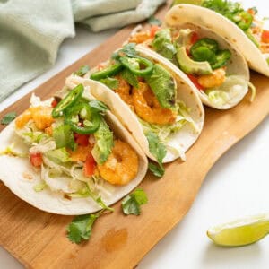 Volcano shrimp tacos on a cutting board topped with cilantro, tomatoes, jalapeno, and avocado.