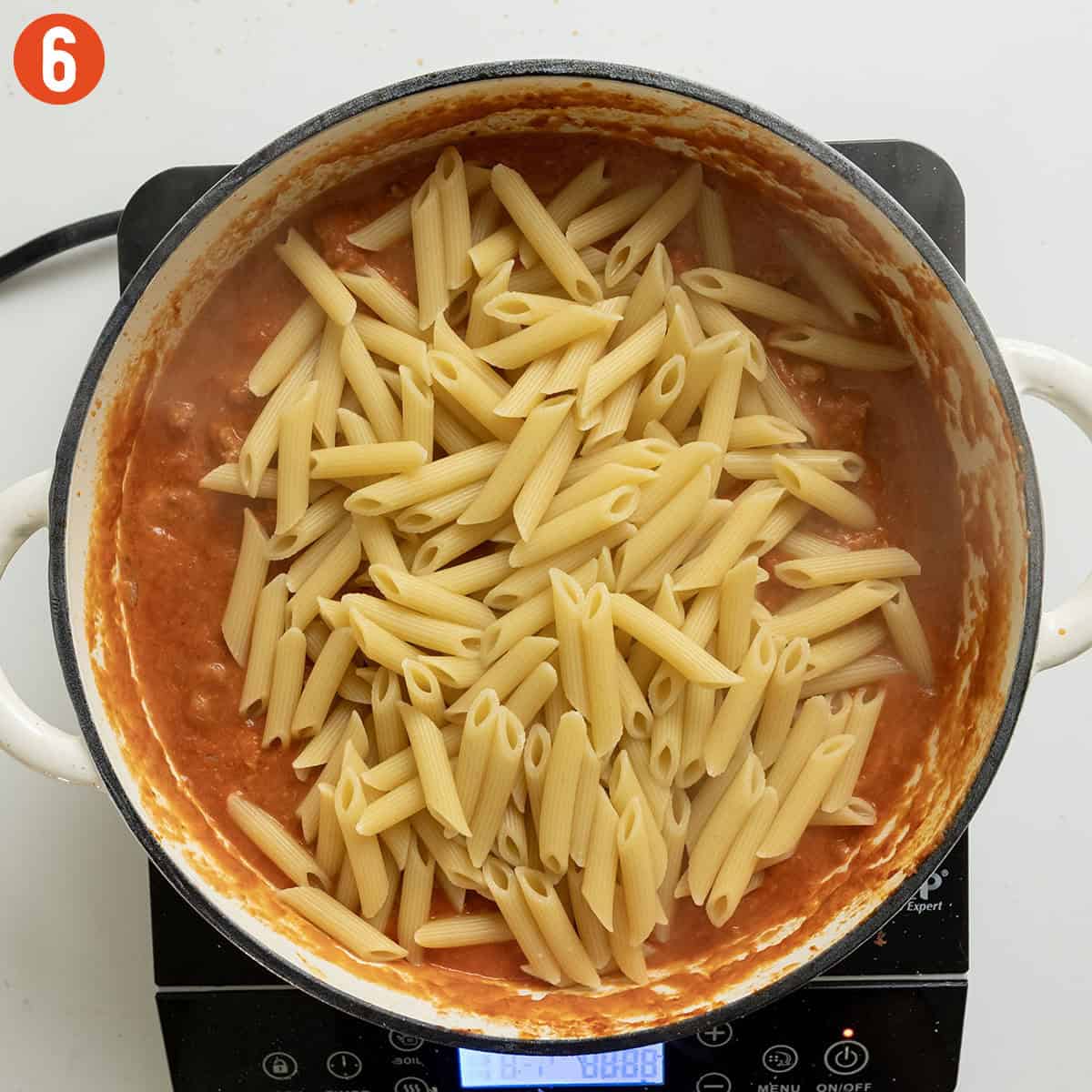 Adding pasta to the pink sauce.