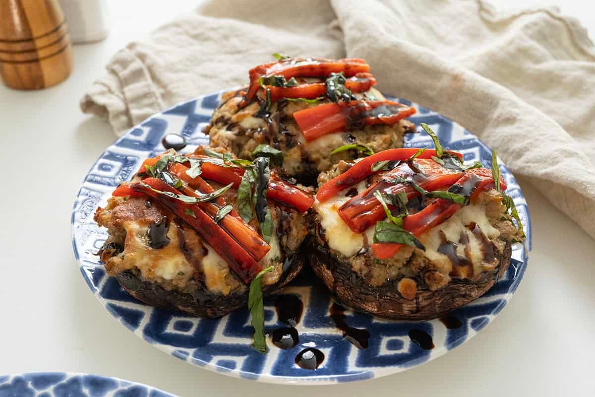 Baked Italian stuffed portobello mushrooms topped with roasted red peppers, basil and balsamic glaze on a plate.
