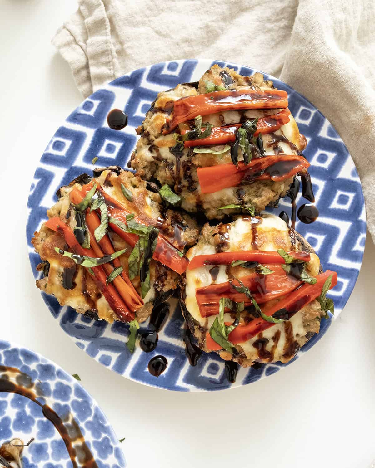 Baked Italian stuffed portobello mushrooms topped with roasted red peppers, basil and balsamic glaze on a plate.