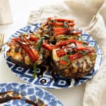 Baked Italian stuffed portobello mushrooms topped with roasted red peppers, basil and balsamic glaze on a plate.