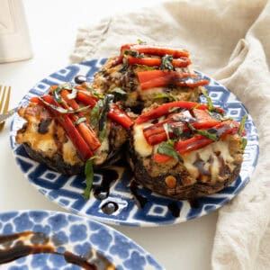 Baked Italian stuffed portobello mushrooms topped with roasted red peppers, basil and balsamic glaze on a plate.