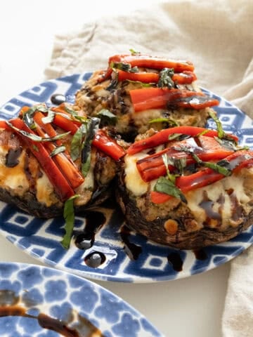 Baked Italian stuffed portobello mushrooms topped with roasted red peppers, basil and balsamic glaze on a plate.