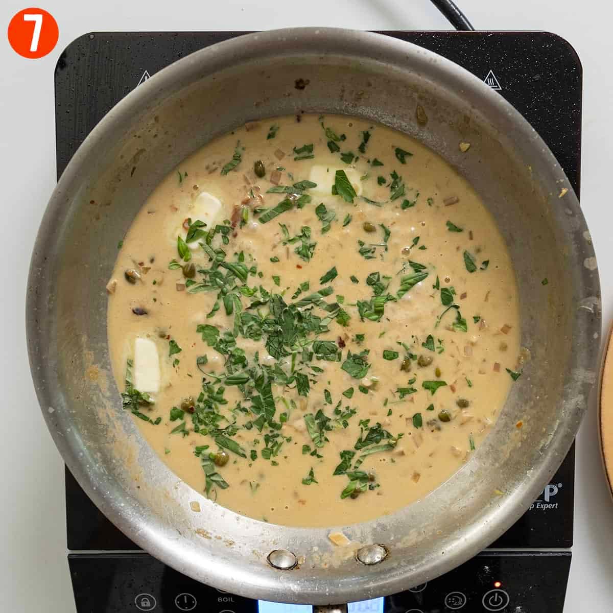 Adding cold butter and parsley to creamy lemon sauce.