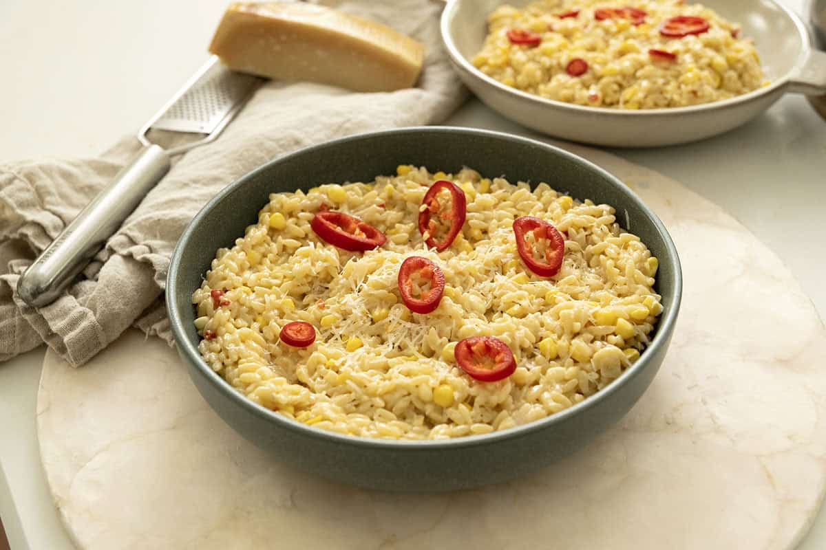 Creamy corn orzo in a bowl topped with red fresno peppers.