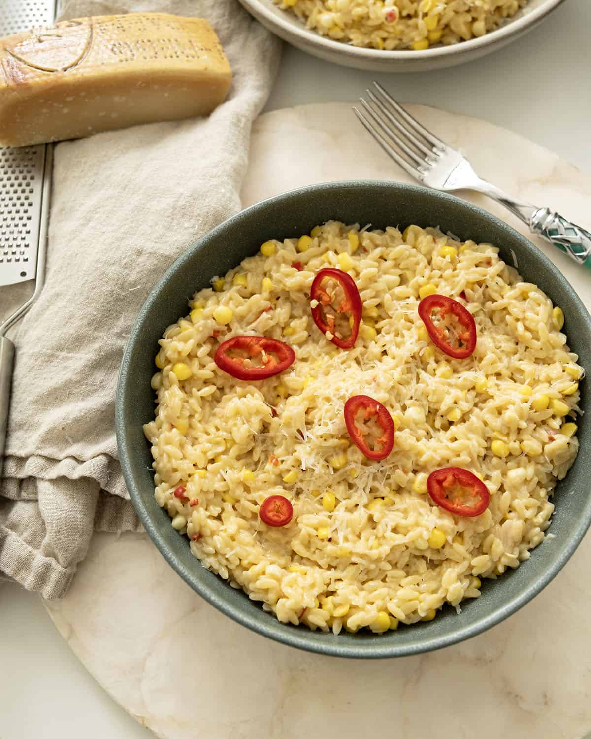 Creamy corn orzo in a bowl topped with red fresno peppers.