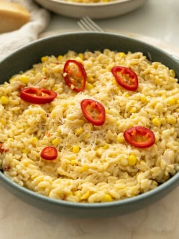 Creamy corn orzo in a bowl topped with red fresno peppers.