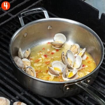Grilled clams transferred to a saucepan on the grill.