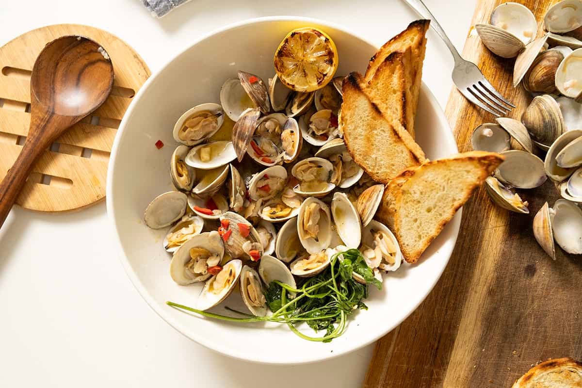 Grilled clams with white wine sauce in a bowl with toasted semolina bread.