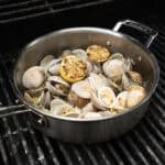 Grilled clams with white wine sauce in a saucepan on the grill.