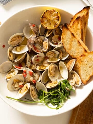 Grilled clams with white wine sauce in a bowl with toasted semolina bread.