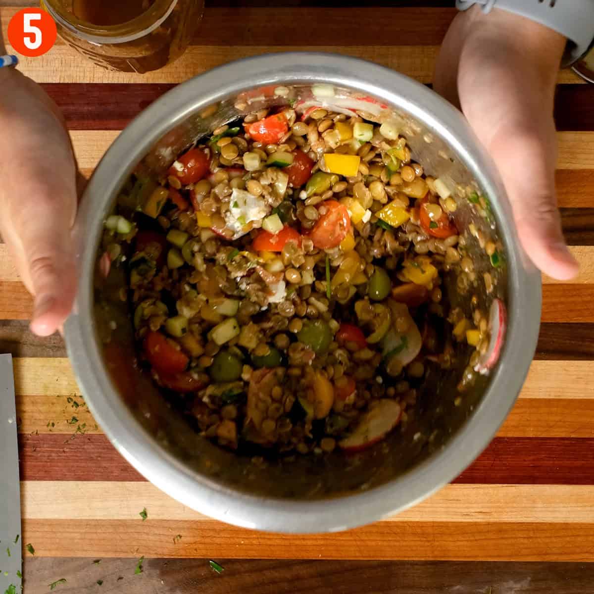 Combining vegetables, lentils, goat cheese, and dressing.
