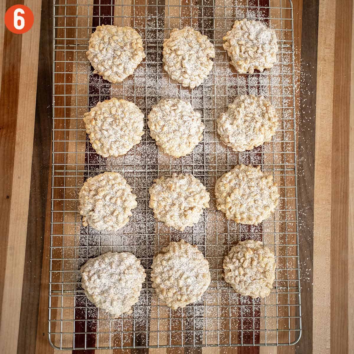 Baked pignoli cookies dusted with powdered sugar on a cooling rack.
