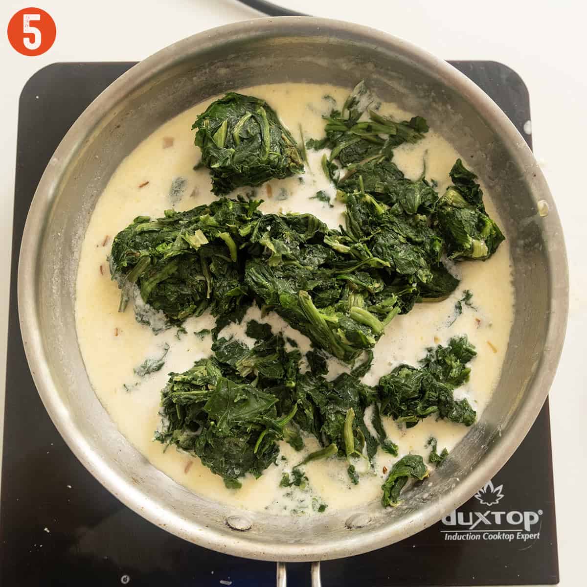 Frozen spinach added to the cream mixture in the pan.