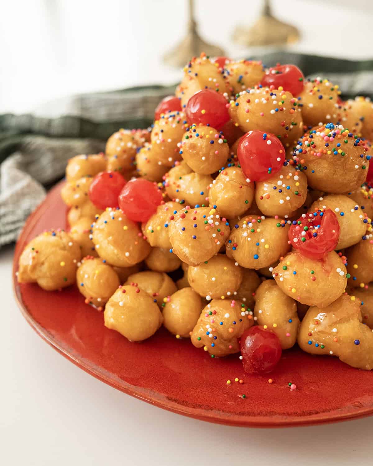 Struffoli piled into a pyramid topped with non-pareils and maraschino cherries.