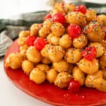 Struffoli piled into a pyramid topped with non-pareils and maraschino cherries.