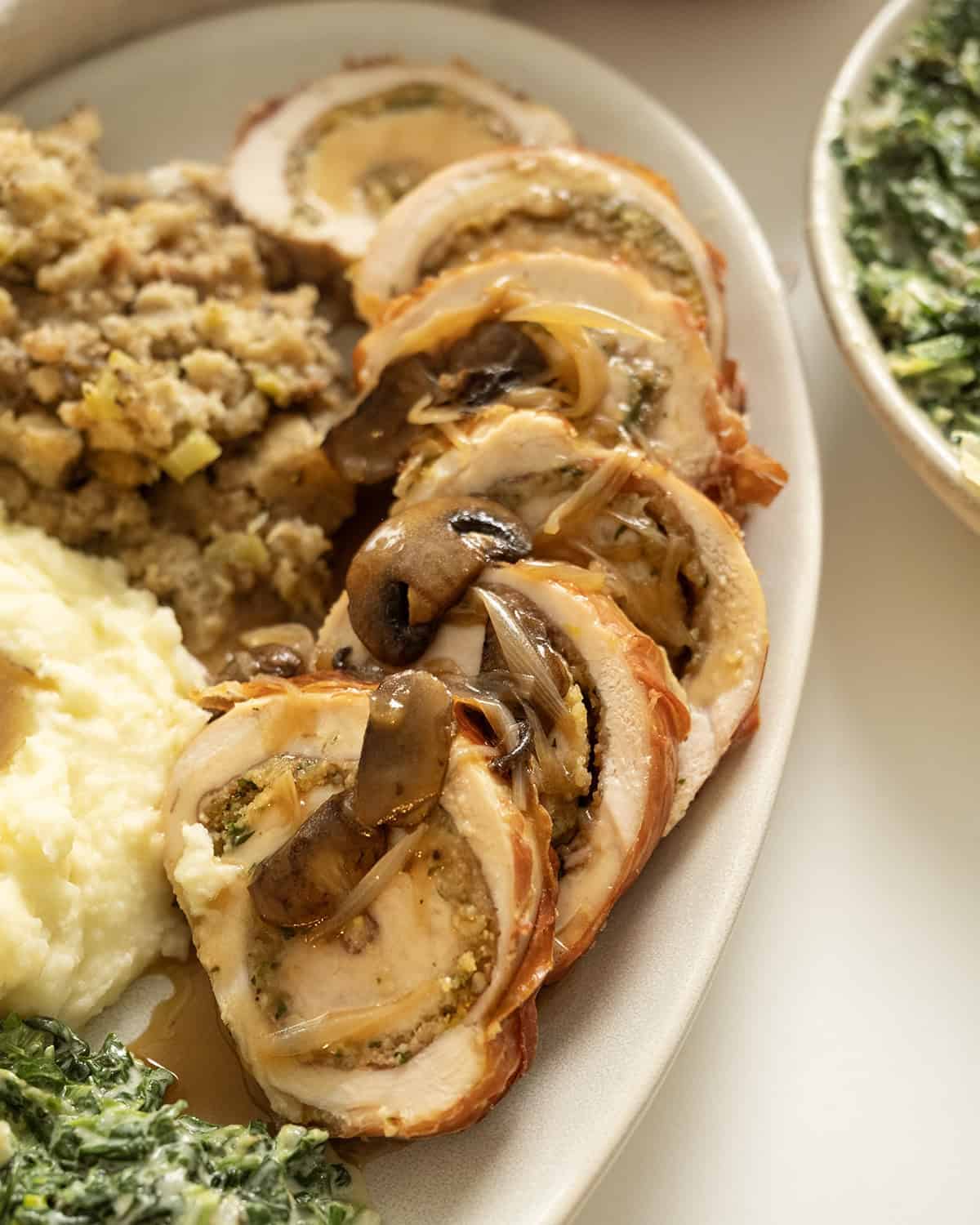 Sliced stuffed turkey breast topped with gravy and on plate with sides.