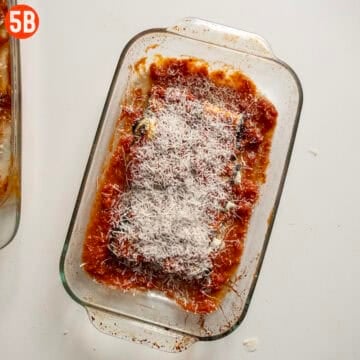 Unbreaded eggplant rollatini topped with sauce and parmigiano in a baking tray.