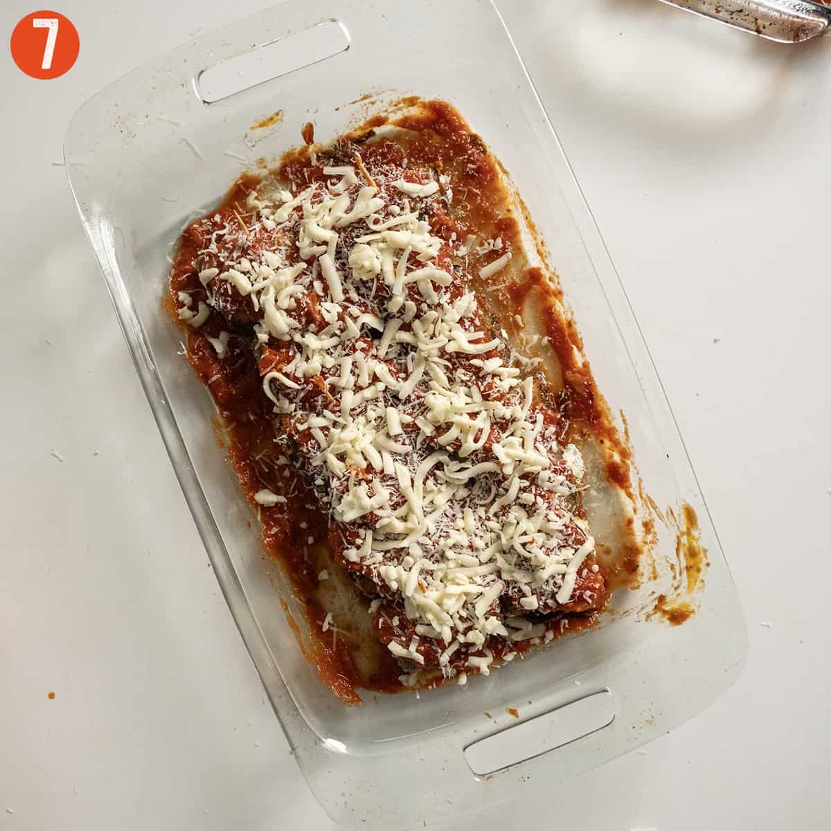 Eggplant rollatini placed in a baking tray with sauce and topped with sauce and cheese.